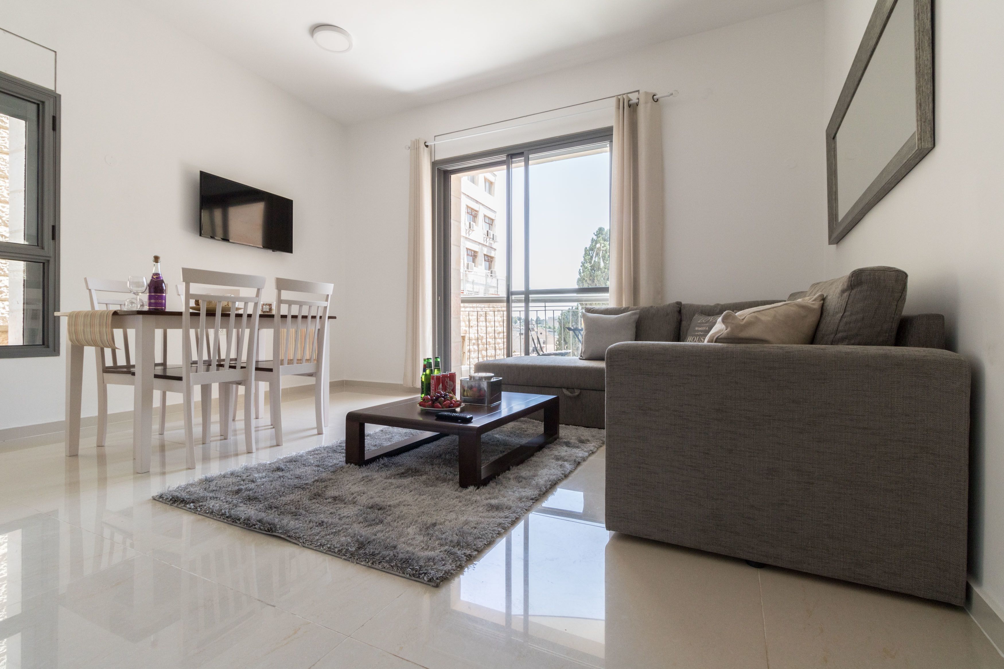 A modern living room with a grey sofa, a coffee table, and a dining area with white chairs.