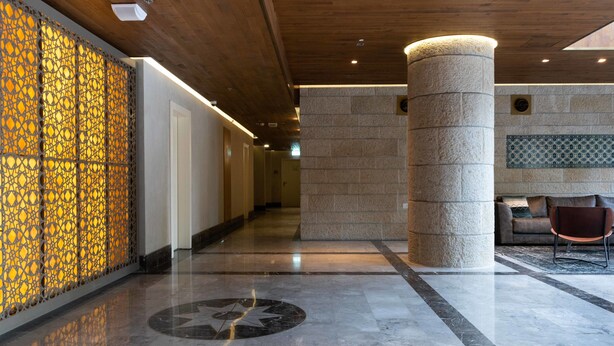 A modern lobby with a wooden ceiling, a decorative wall with a geometric pattern, a large column, and a star-shaped floor design. - The Haneviim Boutique - Isrentals (Jerusalem)