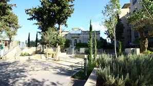 A courtyard with a stone building, a staircase, and a variety of trees. - The Haneviim Boutique - Isrentals (Jerusalem)