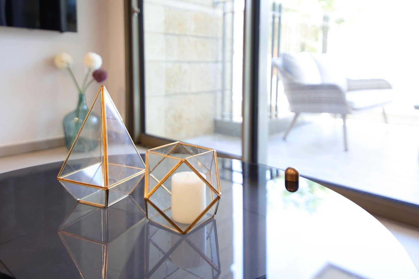 Un interior moderno con una mesa de vidrio que muestra portavelas geométricos y una vela blanca.
