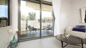 A modern living room with a glass door leading to an outdoor balcony, furnished with wicker chairs and a glass coffee table. - The Haneviim Boutique - Isrentals (Jerusalem)