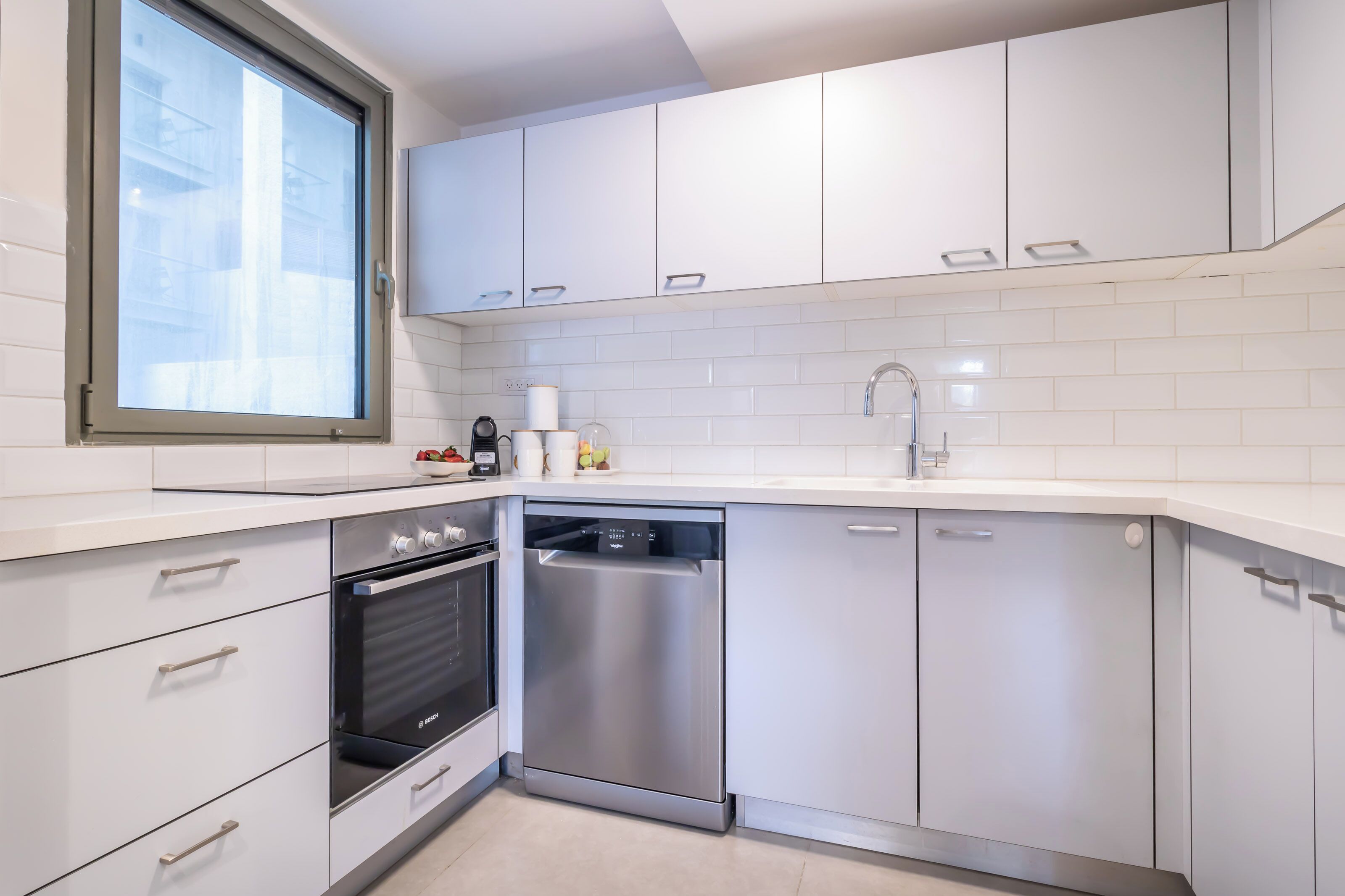 A modern kitchen with white cabinets, a built-in oven, a dishwasher, and a window above the sink.