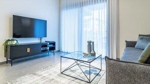 A modern living room with a flat-screen TV, a glass coffee table, a sofa, and a large window with sheer curtains. - The Haneviim Boutique - Isrentals (Jerusalem)