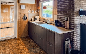 A kitchen with wooden cabinets, a sink, a clock, and a window with a view.