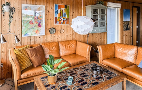 A room with a wooden wall, a brown leather sofa, a coffee table with a plant, and a cabinet.