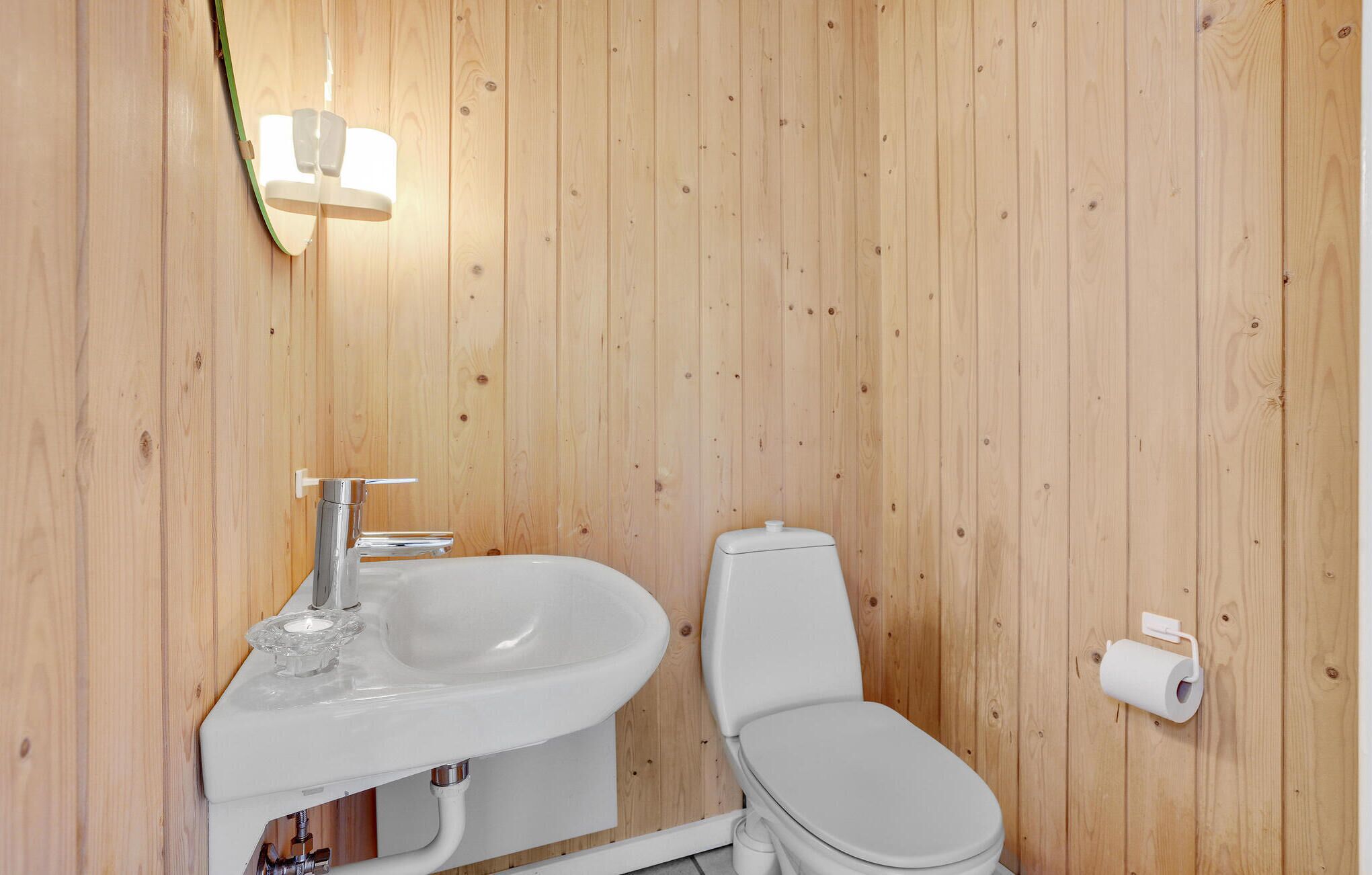 A bathroom with a wooden wall, a white sink, a toilet, and a wall-mounted toilet paper holder.
