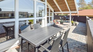 En udendørs terrasse med et bord og stole, en træpergola og belægning i mursten.