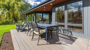 A covered outdoor deck with a table and chairs, surrounded by large windows. - Bend Waterfront Home: Hot Tub, Walk to Town (Bend)