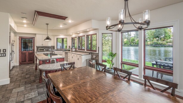 A spacious kitchen with a large island, wooden flooring, and a view of a lake through large windows. - Bend Waterfront Home: Hot Tub, Walk to Town (Bend)