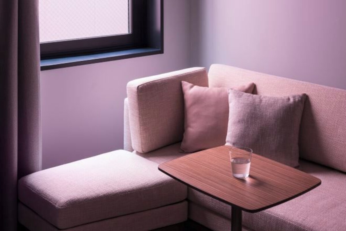 A modern living room with a sofa, a small ottoman, and a wooden side table with a glass of water.