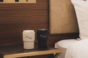 A small bedside table with a white mug and a black travel mug.