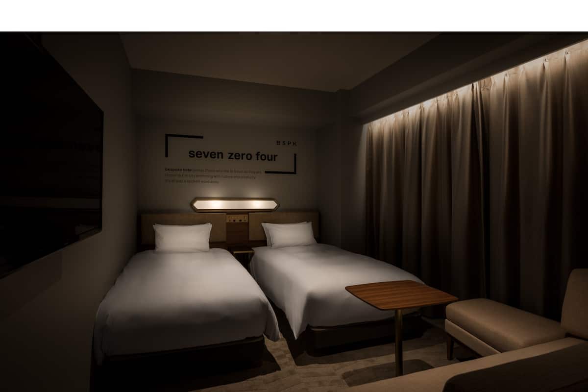 Une chambre d’hôtel avec deux lits, une petite table et une chaise. Un mur porte une inscription indiquant « 704 ».