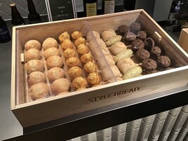 A wooden display case labeled "STYLE BREAD" containing various types of bread.