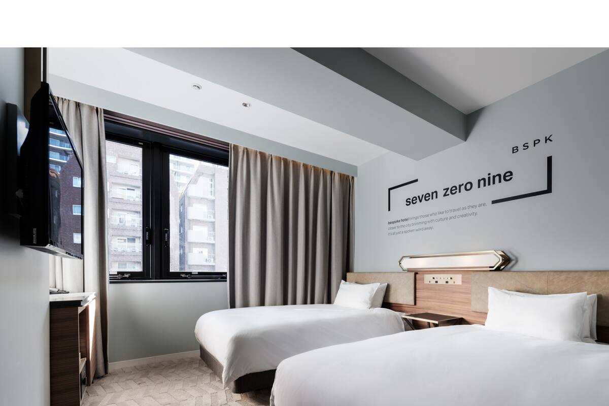 Une chambre d’hôtel avec deux lits, un téléviseur fixé au mur et une fenêtre avec des rideaux.