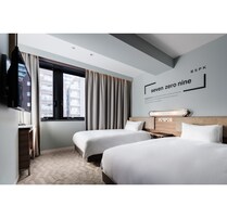A hotel room with two beds, a TV mounted on the wall, and a window with curtains.