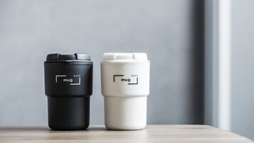 Zwei Reisebecher mit dem Aufdruck 'mug' und 'BSPK', auf einer Holzfläche platziert.