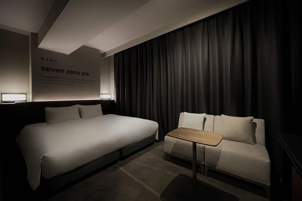 Une chambre d’hôtel avec un grand lit, un petit canapé, une petite table et une lampe fixée au mur.