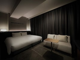 Une chambre d’hôtel moderne avec un grand lit, un petit canapé, une table de chevet et un téléviseur fixé au mur.
