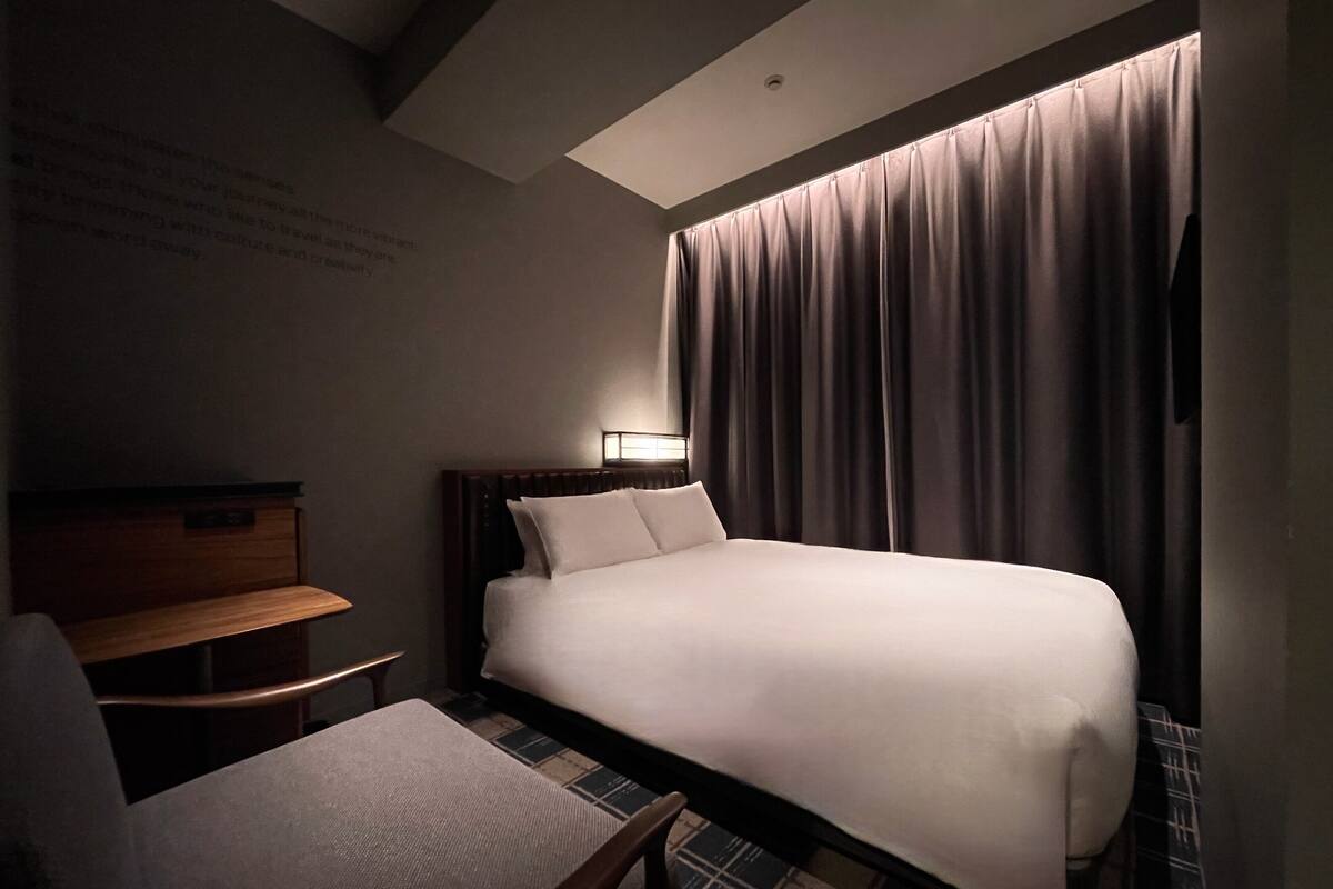 Une chambre d’hôtel avec un grand lit, une table de chevet en bois, une chaise et une lampe fixée au mur.