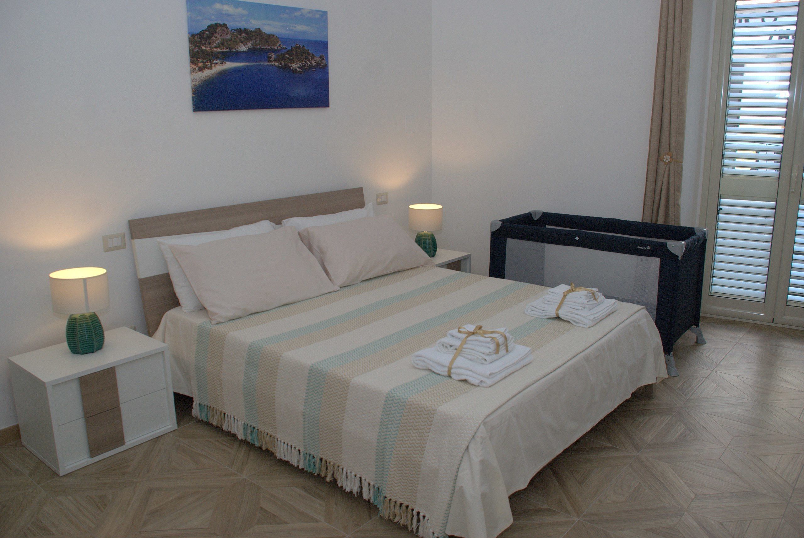 Un letto ben rifatto con coperta a righe, una lampada da comodino e un asciugamano piegato sul tavolino.
