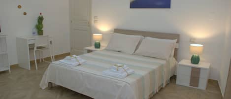 A neatly arranged bedroom with a bed, bedside tables, a desk, and a chair.