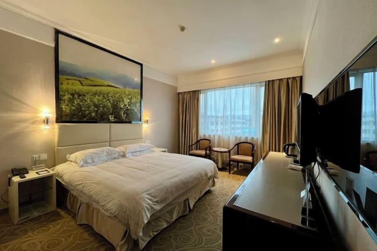 A hotel room with a large bed, a desk, a chair, a TV, and a painting on the wall.
