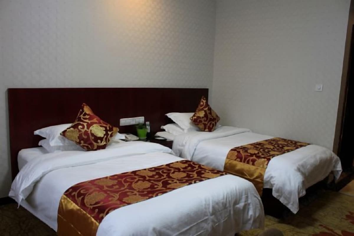 A hotel room with two single beds, each with a red and white bedspread, a wooden headboard, and a nightstand with a green bottle.