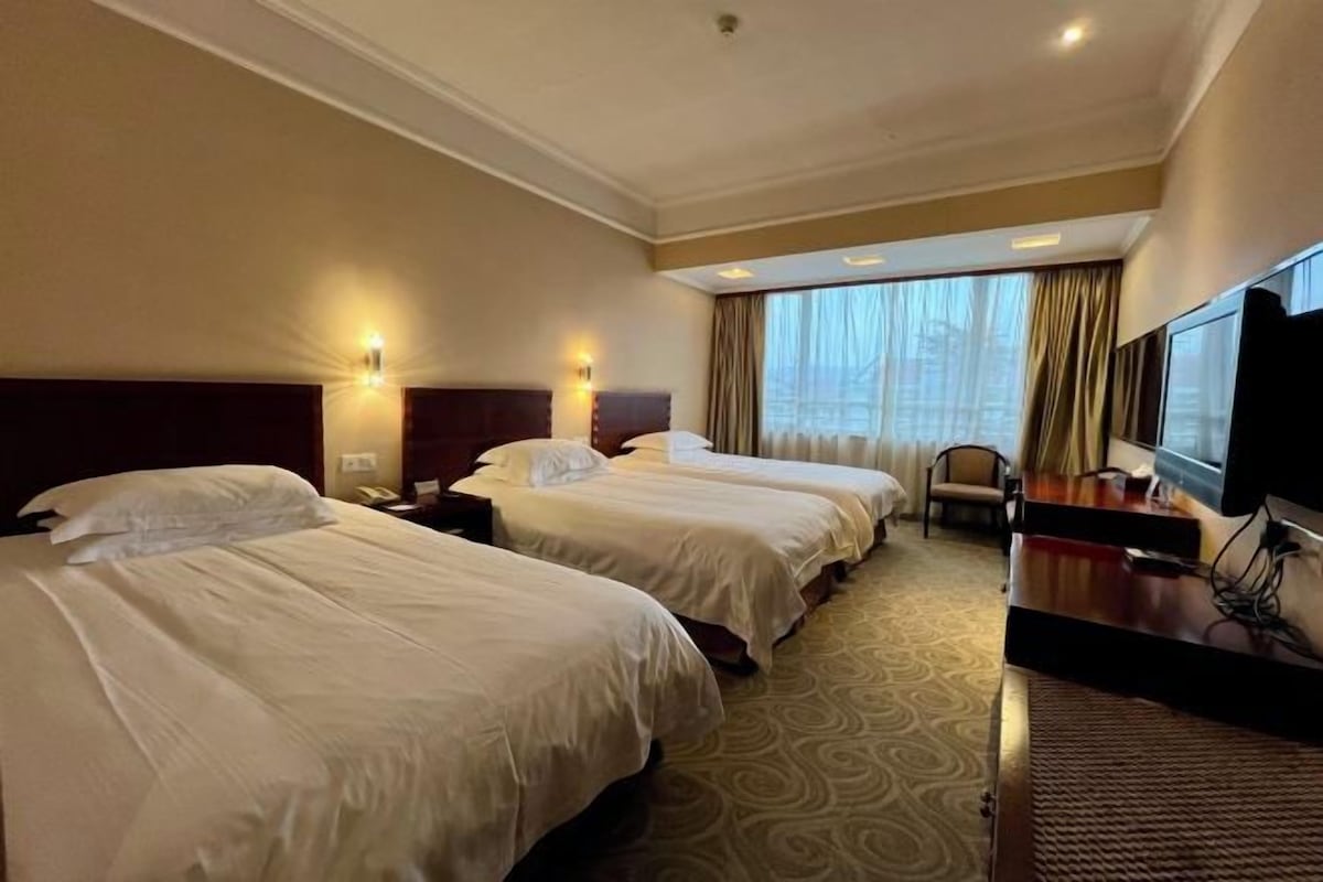 A hotel room with two beds, a desk, a television, and a window with curtains.
