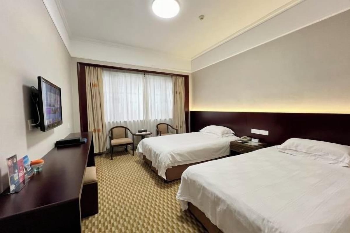 A hotel room with two beds, a desk with a chair, a television, and a window with curtains.