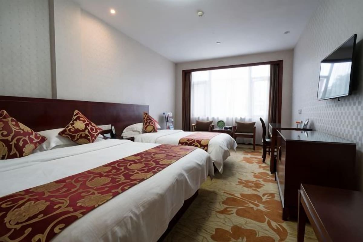 A hotel room with two beds, a desk, and a television.