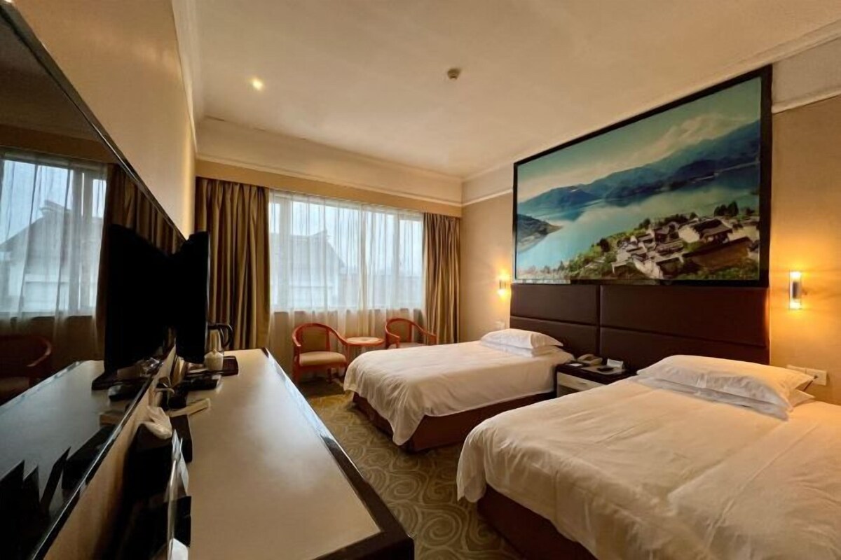 A hotel room with two beds, a desk, a TV, and a painting on the wall.