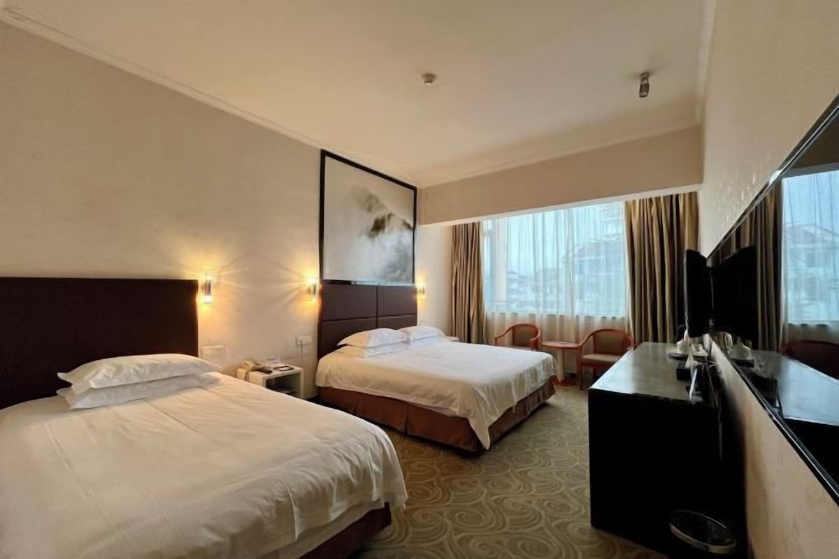 A hotel room with two beds, a desk, a chair, and a large mirror.