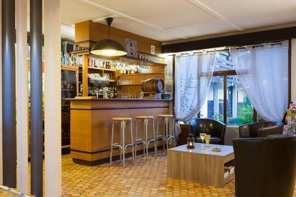 A bar area with stools, a counter with bottles, and a view through sheer curtains.