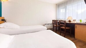 Een hotelkamer met twee bedden, een bureau met stoel, een televisie en een raam met gordijnen.
