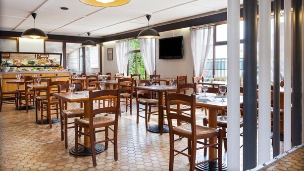 Een restaurant met houten tafels en stoelen, een betegelde vloer, hanglampen en een buffet.