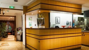 Een receptiezone met een houten receptiebalie, een potplant en een lijst met een citaat aan de muur.