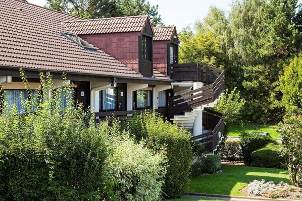 Ein zweigeschossiges Haus mit rotem Ziegeldach, einem Balkon und einem gepflegten Garten.