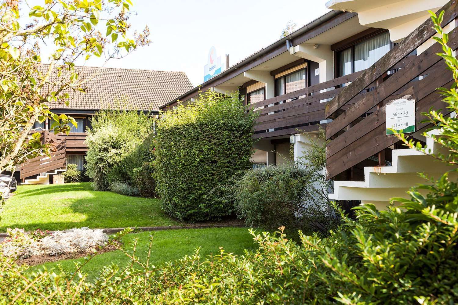 A hotel with a well-maintained garden, a wooden staircase, and a sign indicating room numbers.