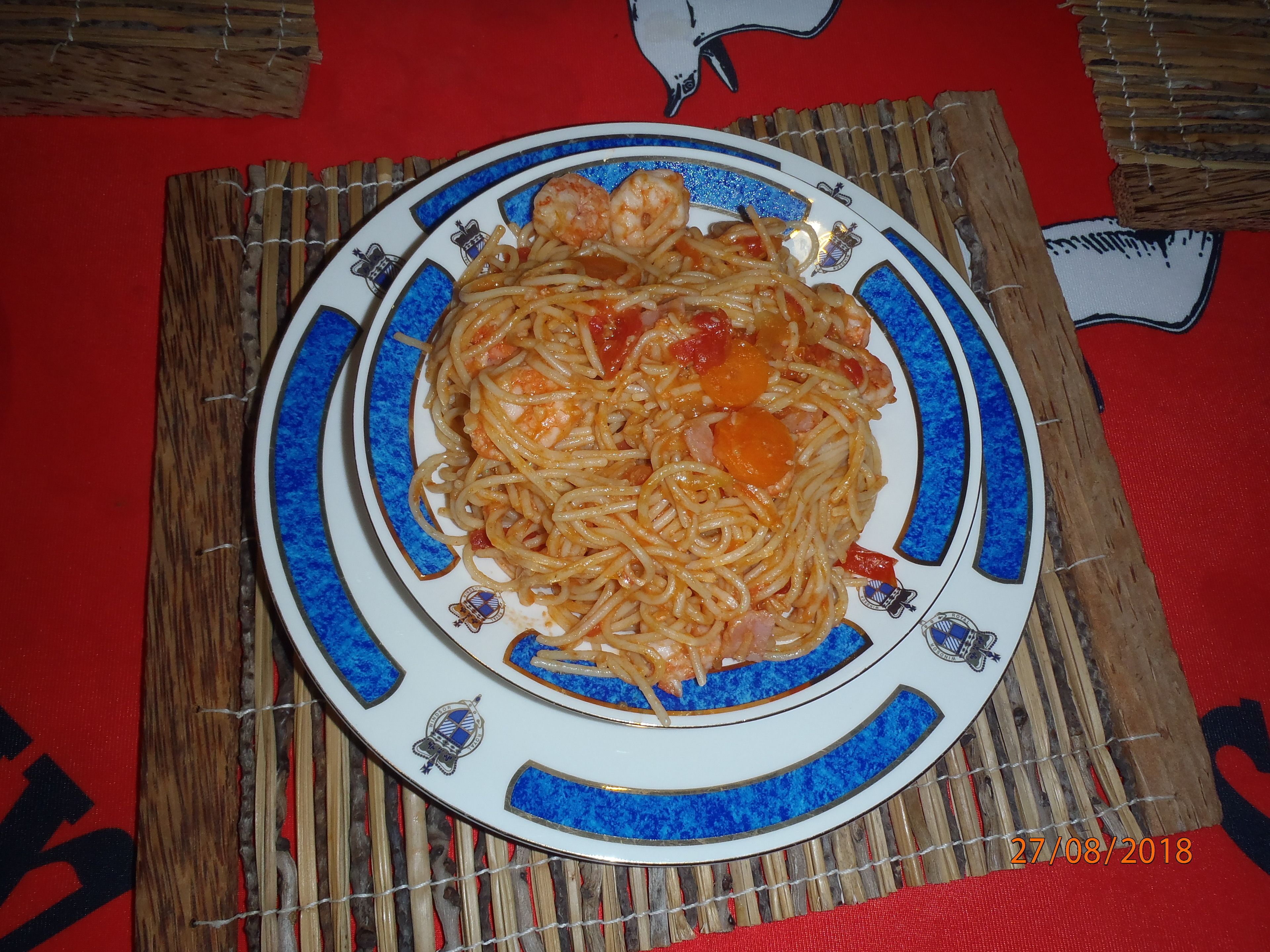 Un piatto di spaghetti con gamberi e verdure su un piatto decorativo.