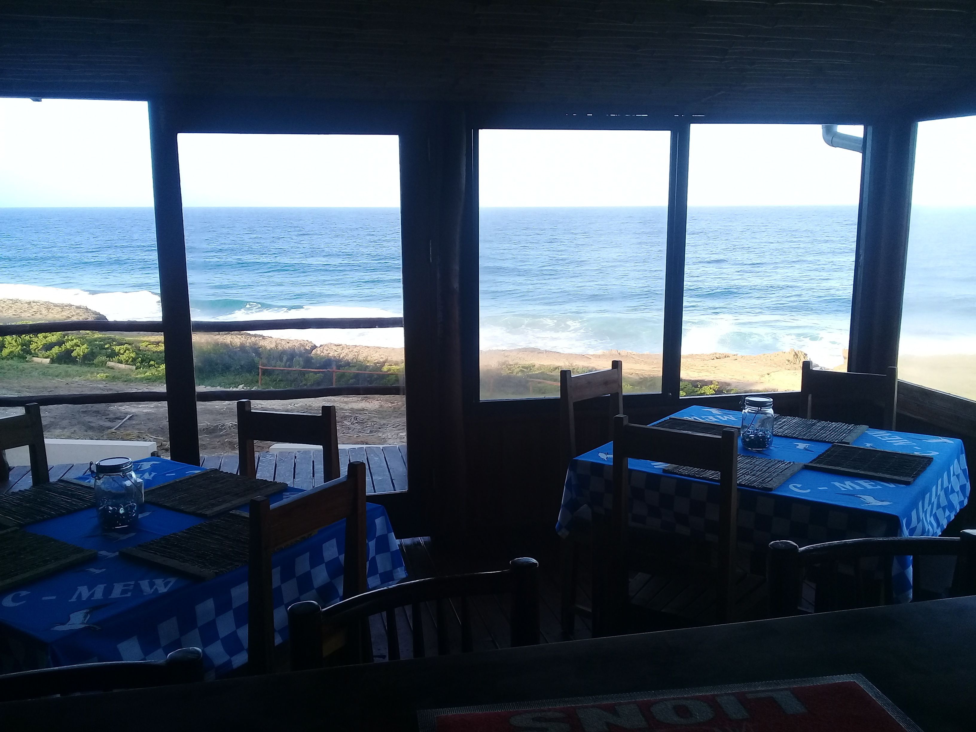 A restaurant with tables and chairs, large windows with ocean views, and a sign reading "SNOW".