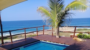 A pool area with a view of the ocean, wooden deck, and a palm tree. - C-Mew Guesthouse (Inhambane)