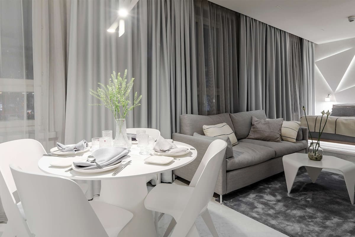 Un salon moderne avec un canapé gris, des chaises blanches et une table à manger dressée pour quatre personnes.