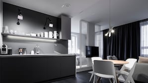 Een moderne keuken met een donker aanrecht, een koffieapparaat en een spoelbak. Er is een zithoek met een tafel en stoelen, en een tv aan de wand bevestigd.