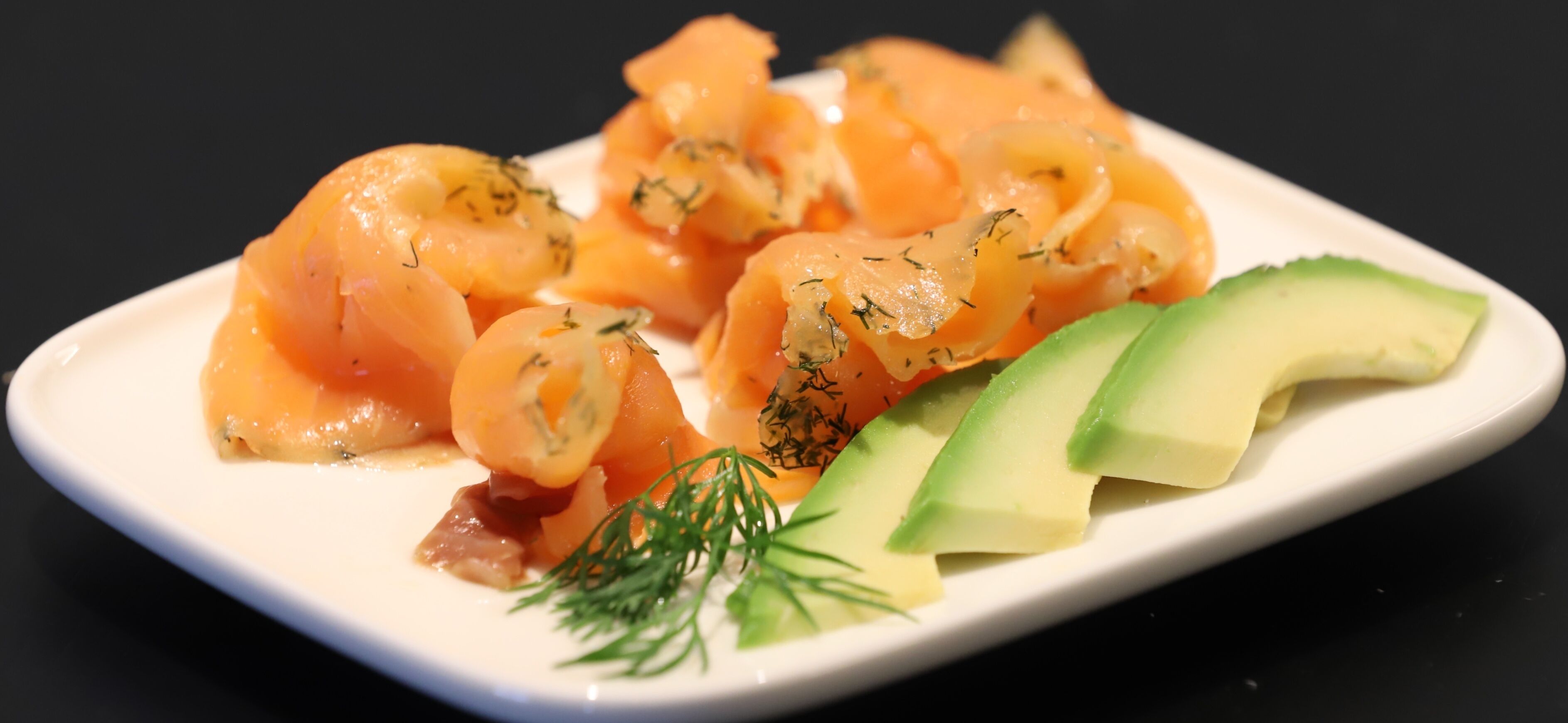 A plate of smoked salmon with dill and avocado slices.