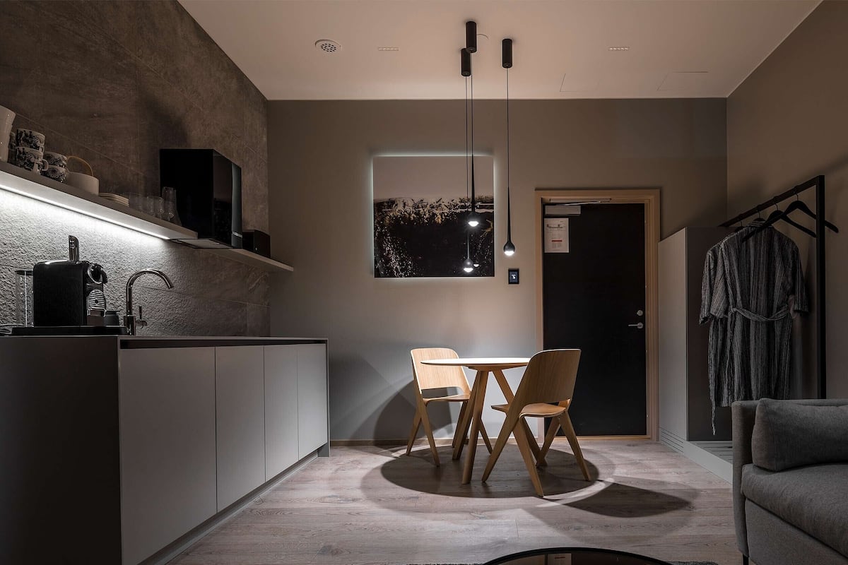 Une cuisine moderne dotée d’une cuisinière intégrée, d’un coin repas avec une table et des chaises en bois, et d’un canapé gris.
