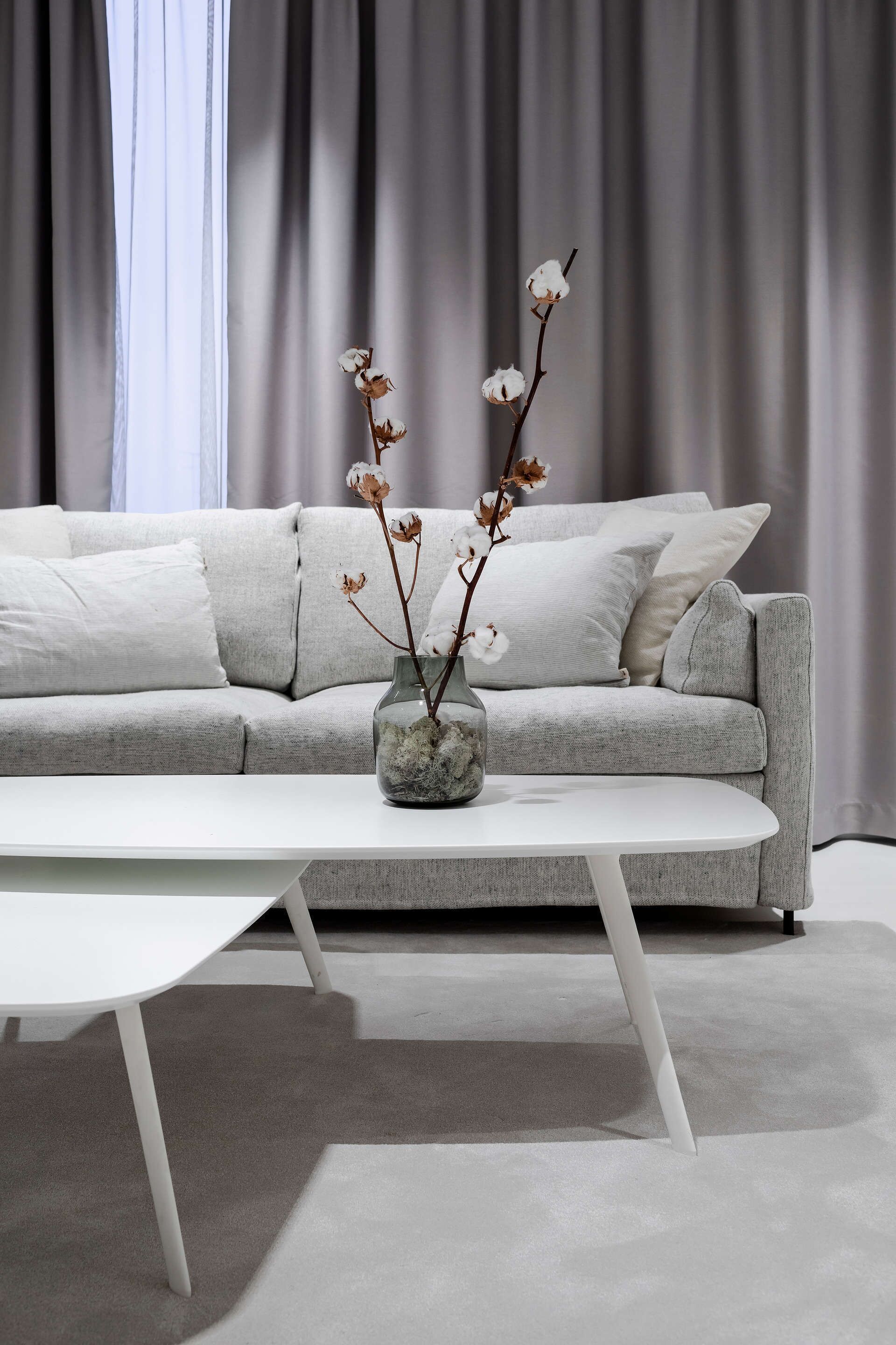 A modern living room with a grey sofa, white cushions, and a white coffee table.