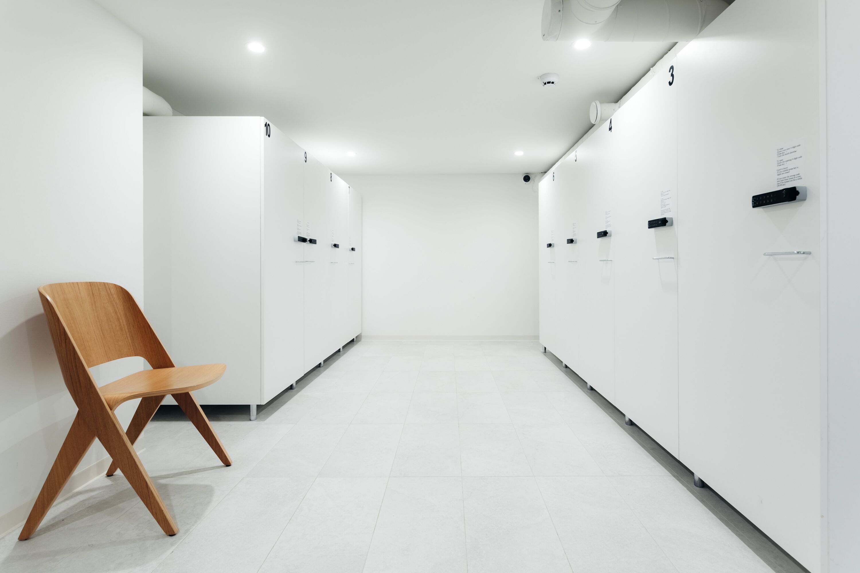 Un pasillo moderno y minimalista con taquillas, una silla de madera y un suelo blanco e impecable.