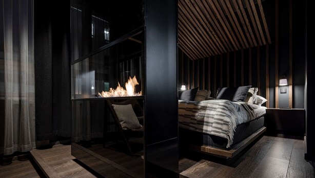 Een moderne slaapkamer met een bed, nachtkastjes en een open haard.