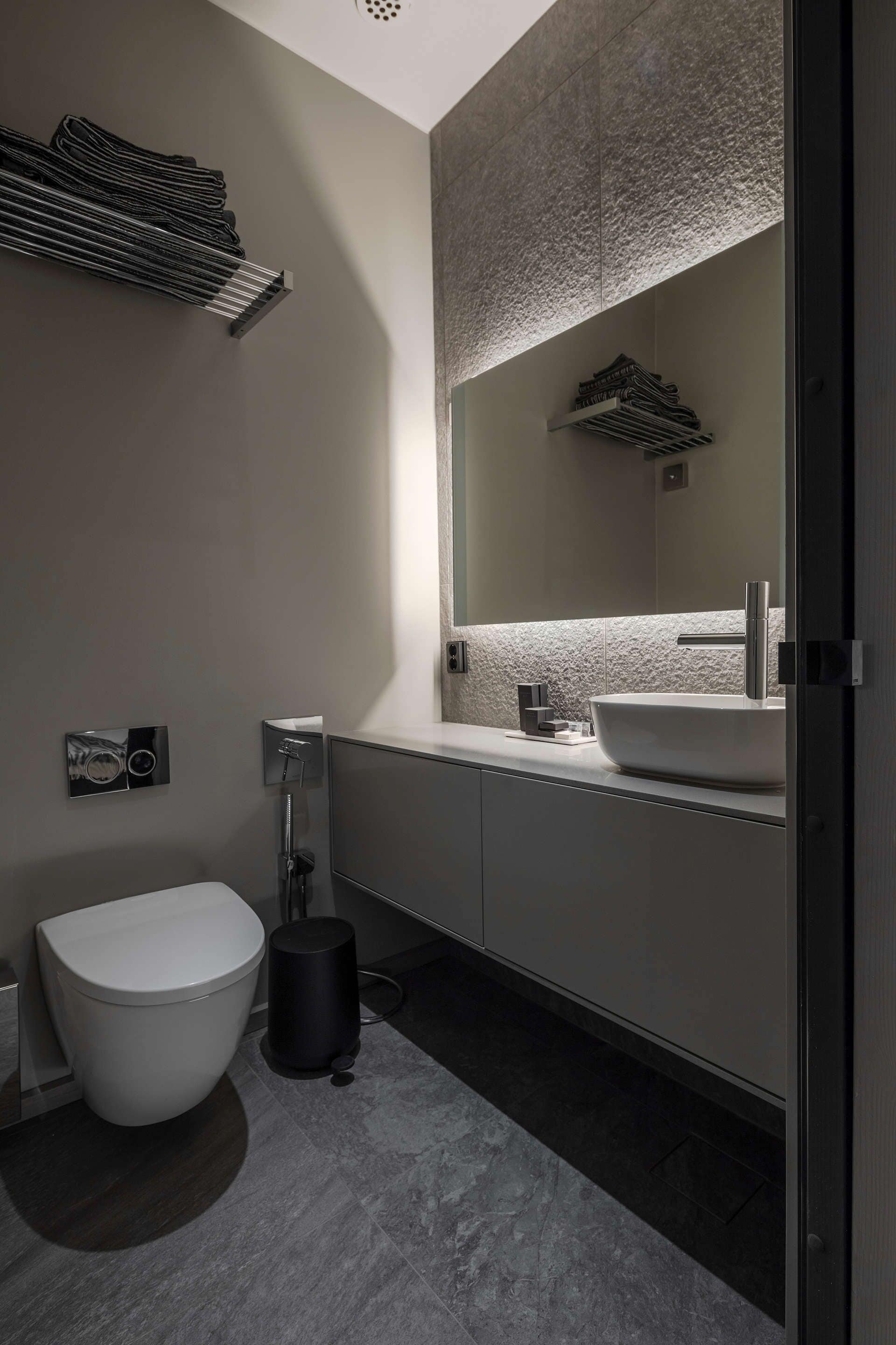 Een moderne badkamer met een wit toilet, een grote spiegel en een witte wastafel.