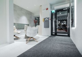 Un área de recepción moderna con puerta de cristal, mostrador de recepción y zona de estar con sillas.